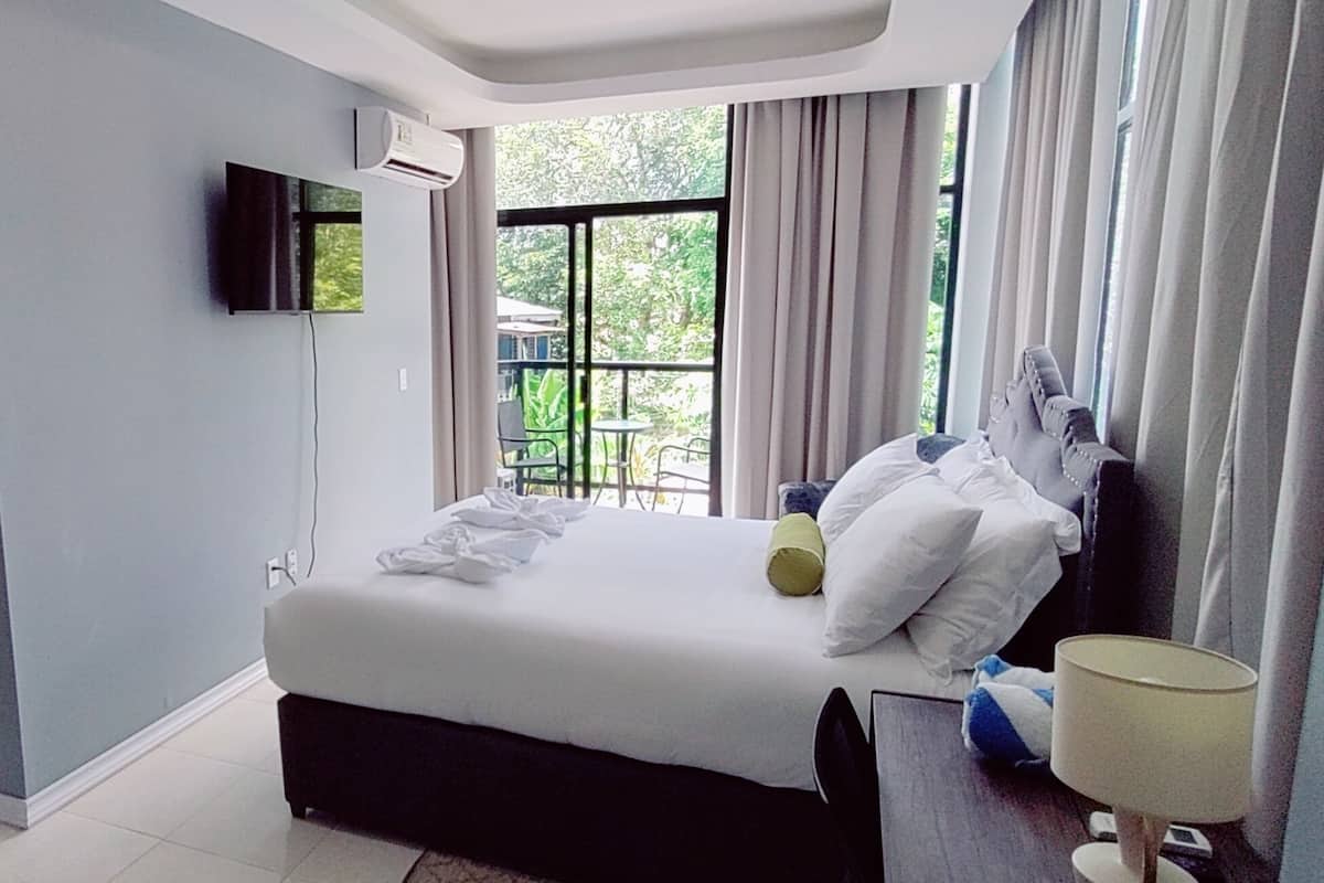 Ein Hotelzimmer mit Bett, Fernseher, Fenster mit Vorhängen, Bad mit Waschbecken und Tür.