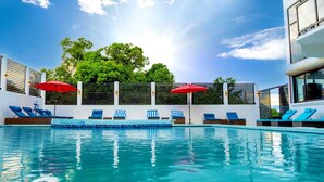 A swimming pool with lounge chairs and umbrellas, surrounded by a white wall and trees. - The Alexandria Marquis Hotel & Resorts (San Ignacio)