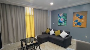 A living room with a sectional sofa, a glass coffee table, a flat-screen TV, and two paintings on the wall. - The Alexandria Marquis Hotel & Resorts (San Ignacio)