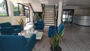 A modern lobby with teal chairs, a glass coffee table, a staircase, and a reception desk. - The Alexandria Marquis Hotel & Resorts (San Ignacio)