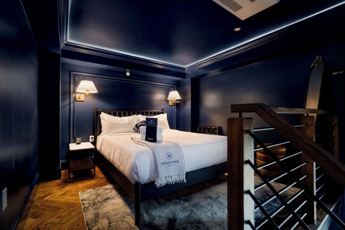 Ein Hotelzimmer mit Bett, Nachttischen, Holzboden, Treppe und Wandleuchten.