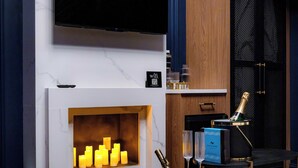 Uma sala de estar moderna com lareira, televisão na parede e área de bar com uma garrafa de champanhe.