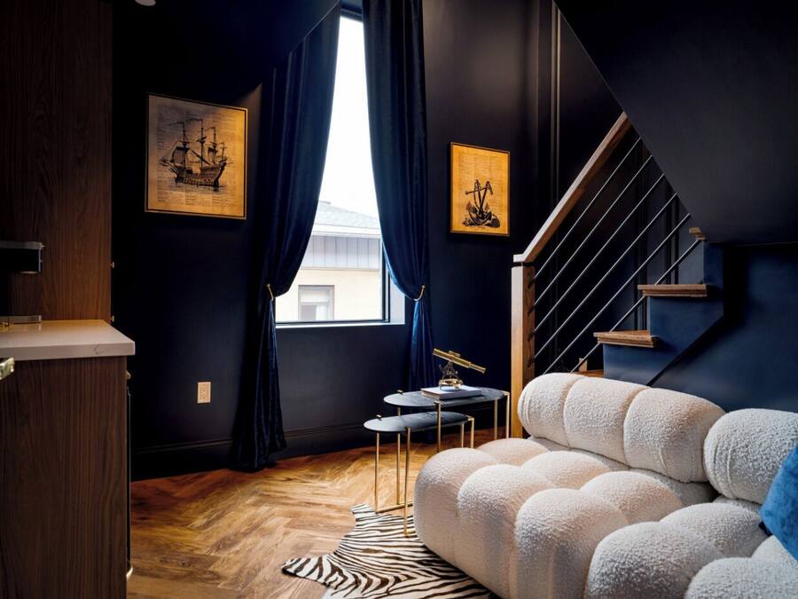 Una sala de estar moderna con una pared azul oscuro, una puerta de madera, un tapete con estampado de cebra, un sofá blanco, una pequeña mesa redonda con un telescopio y una escalera.