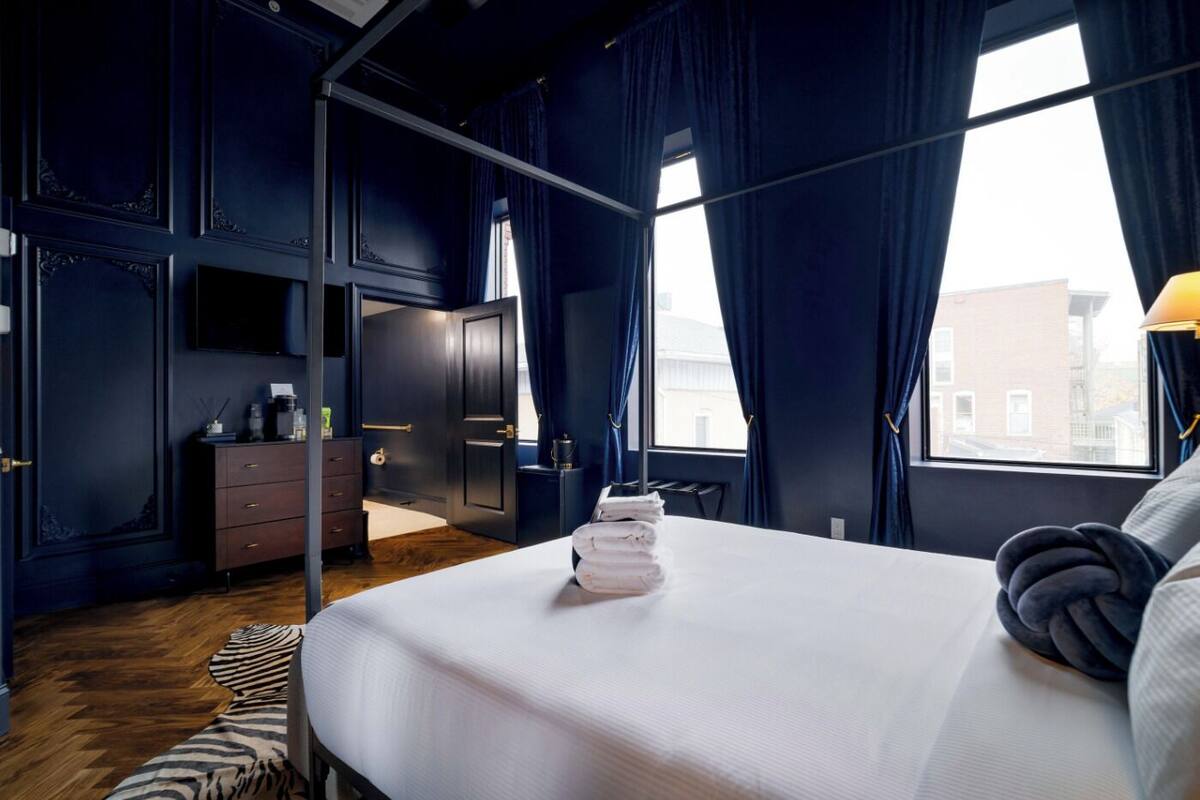 Ein modernes Hotelzimmer mit einem großen Bett, dunkelblauen Wänden und Blick auf die Stadt.