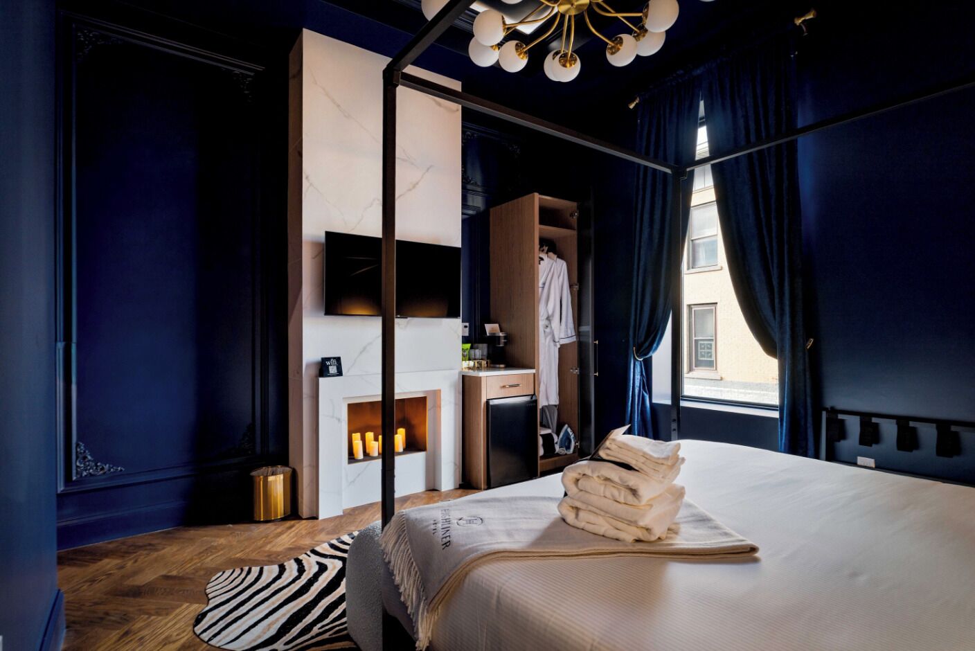 A modern hotel room with a large bed, a wardrobe, a desk, and a seating area with candles.