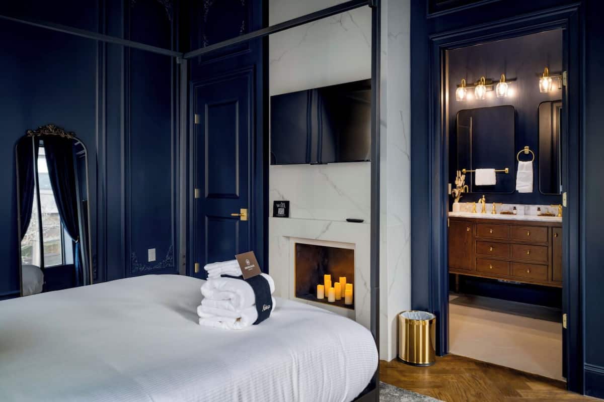 Ein Schlafzimmer mit einem großen Bett, einem Kamin, einem Schminktisch mit Spiegel und einer Tür zu einem Badezimmer.