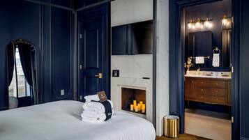 A bedroom with a large bed, a fireplace, a vanity with a mirror, and a door leading to a bathroom.