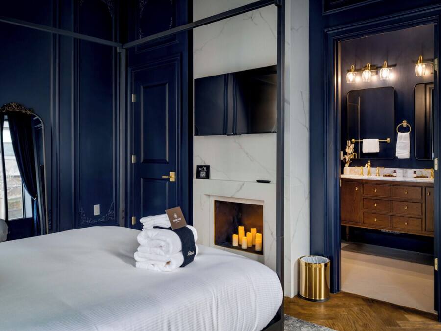A bedroom with a large bed, a fireplace, a vanity with a mirror, and a door leading to a bathroom.