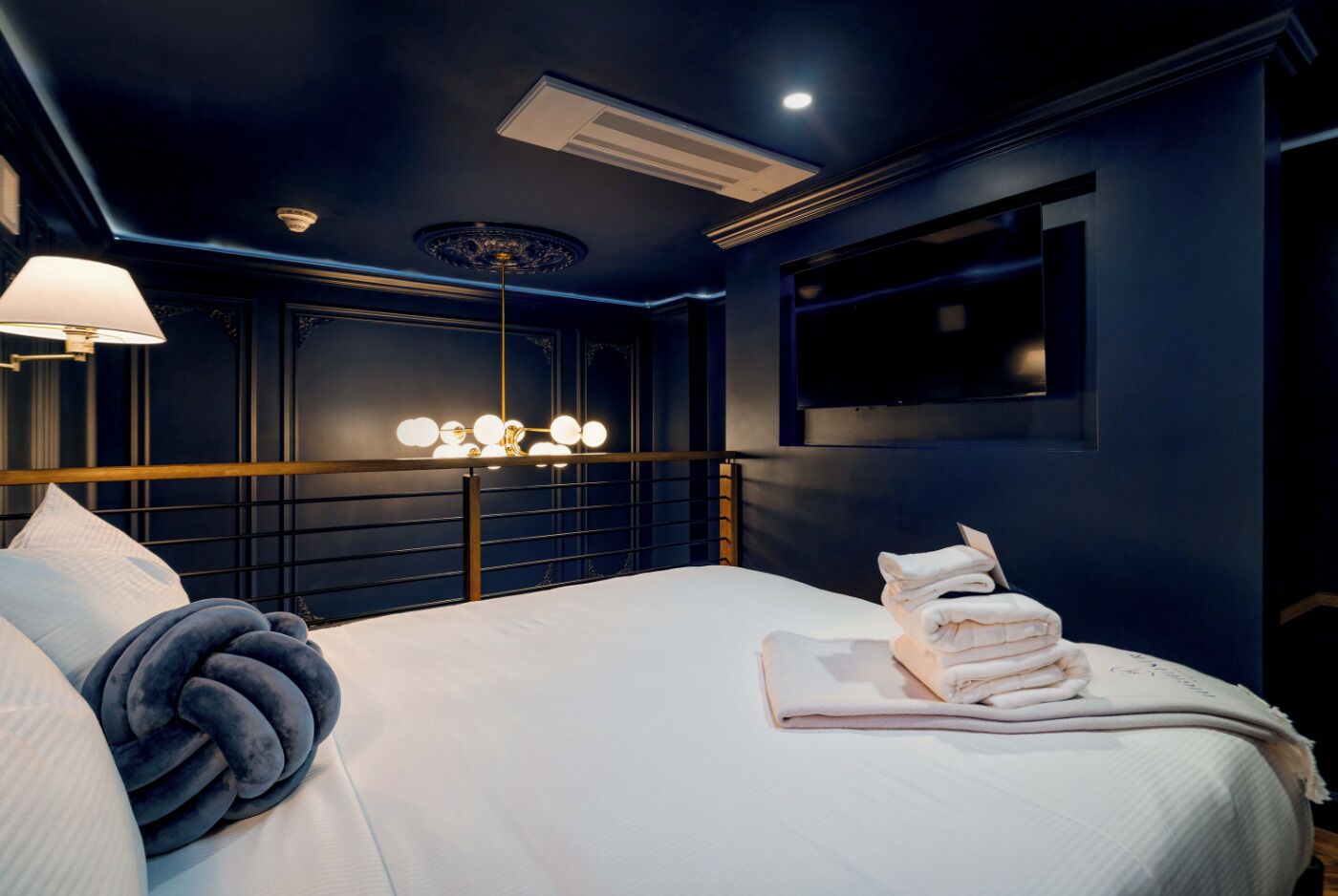 Habitación de hotel con una cama grande, cabecera con luces, televisor montado en la pared y lámpara de techo.