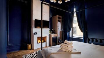 Une chambre d’hôtel moderne avec un grand lit, un plancher en bois, un tapis à motifs zébrés, une cheminée et une vue sur la ville par la fenêtre.
