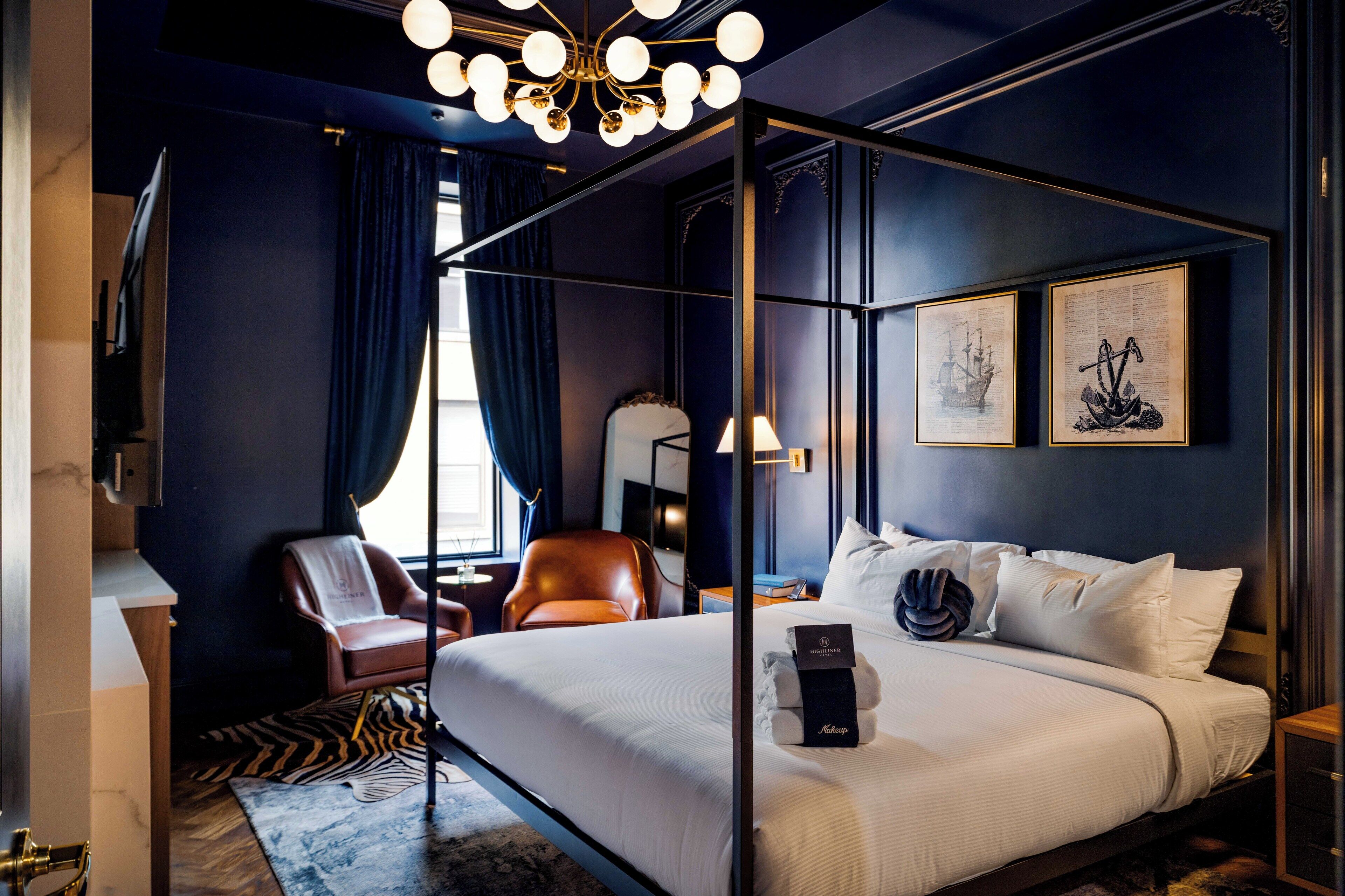 Ein Bett mit Baldachin, ausgestattet mit weißen Leinen, ein Ledersessel, ein Schreibtisch mit Lampe und zwei gerahmte Kunstwerke an der Wand.