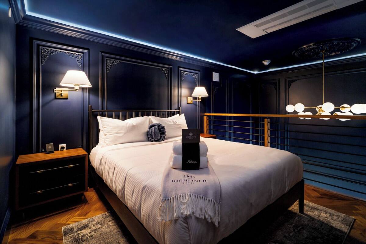Ein modernes Schlafzimmer mit blauer Wand, einem Holz-Kopfteil, weißer Bettdecke und zwei Nachttischlampen.