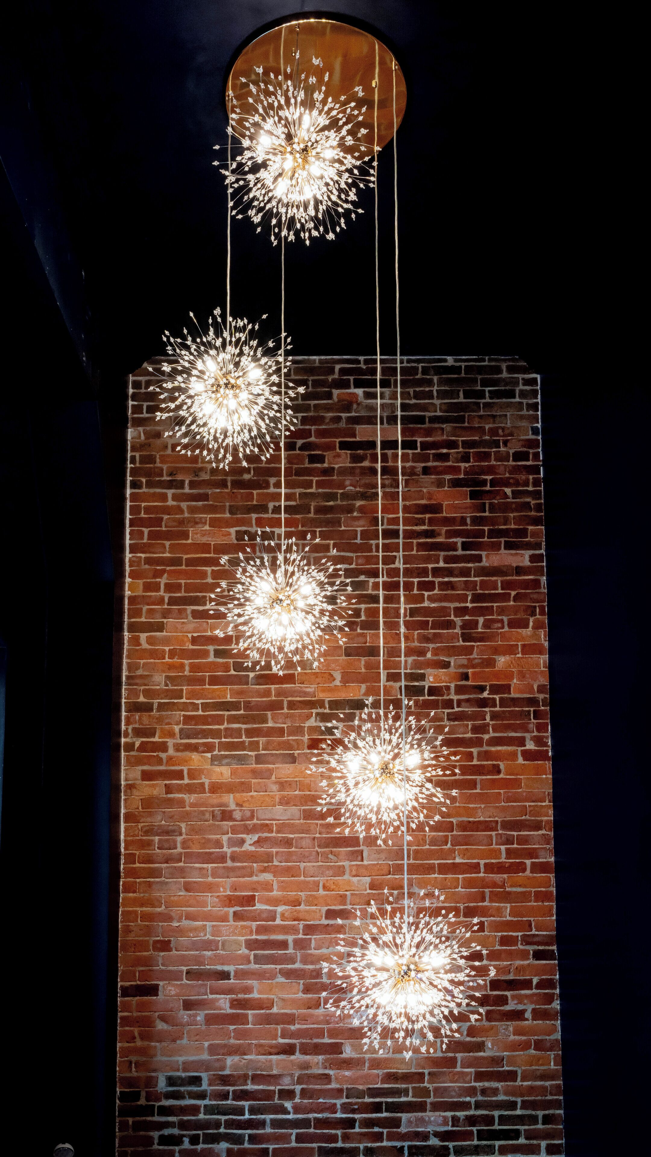 A modern chandelier with multiple hanging lights against a brick wall.