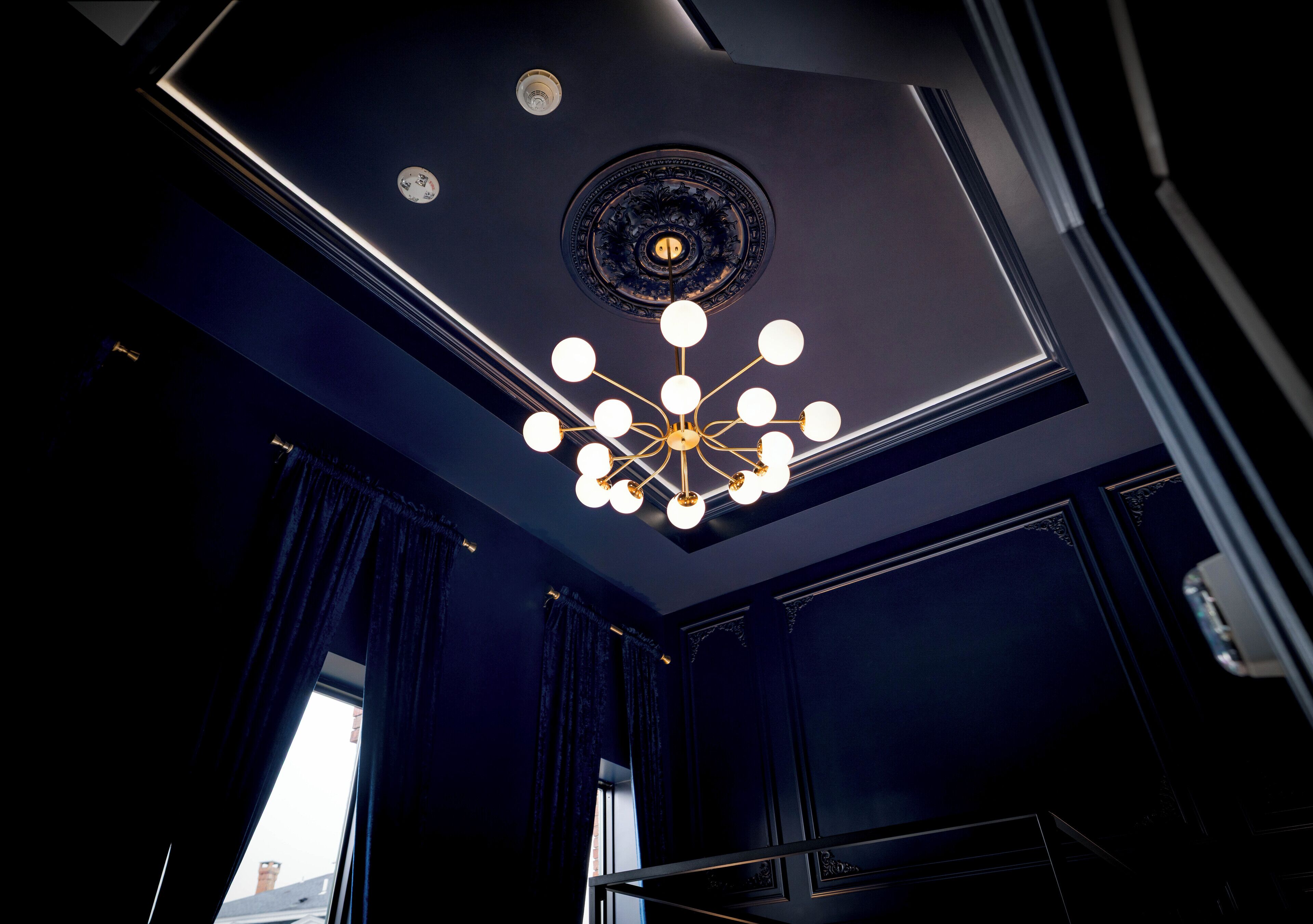 A room with a dark blue ceiling, a decorative circular light fixture, and a window with curtains.