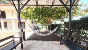 A covered outdoor seating area with a hammock, gravel ground, and a building in the background. - Studio/Pool/WIFI-Full kitchen-A/C-Large Beach-Sunsets-Surf and Relax** (Provincia de Guanacaste)