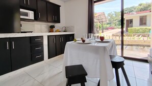 A modern kitchen with dark cabinets, a white countertop, and a dining area with a table set for two. - Studio/Pool/WIFI-Full kitchen-A/C-Large Beach-Sunsets-Surf and Relax** (Provincia de Guanacaste)