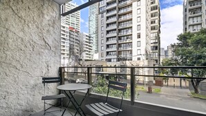 A balcony with a table and two chairs, overlooking a street with tall buildings and a clear sky. - Chic 1-bed South Melbourne Unit With Pool & Gym (Melbourne)