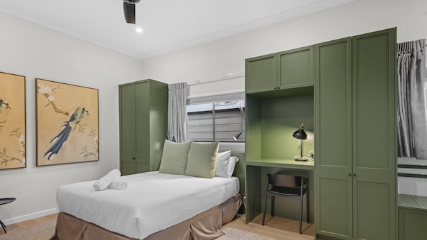 Ein Schlafzimmer mit Bett, grünem Wandschrank, Schreibtisch, Stuhl und Kunstwerk.