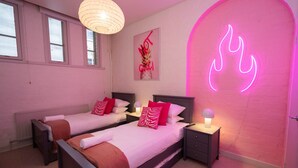 Ein Hotelzimmer mit zwei Betten, einer pinkfarbenen Neonreklame und einem weißen Heizkörper.