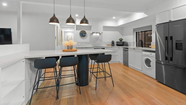 Een moderne keuken met een centraal eiland, barkrukken, hanglampen, een klok en ingebouwde apparatuur.