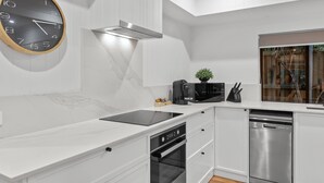 Een moderne keuken met witte kastjes, een zwarte klok, een fornuis en een vaatwasser.