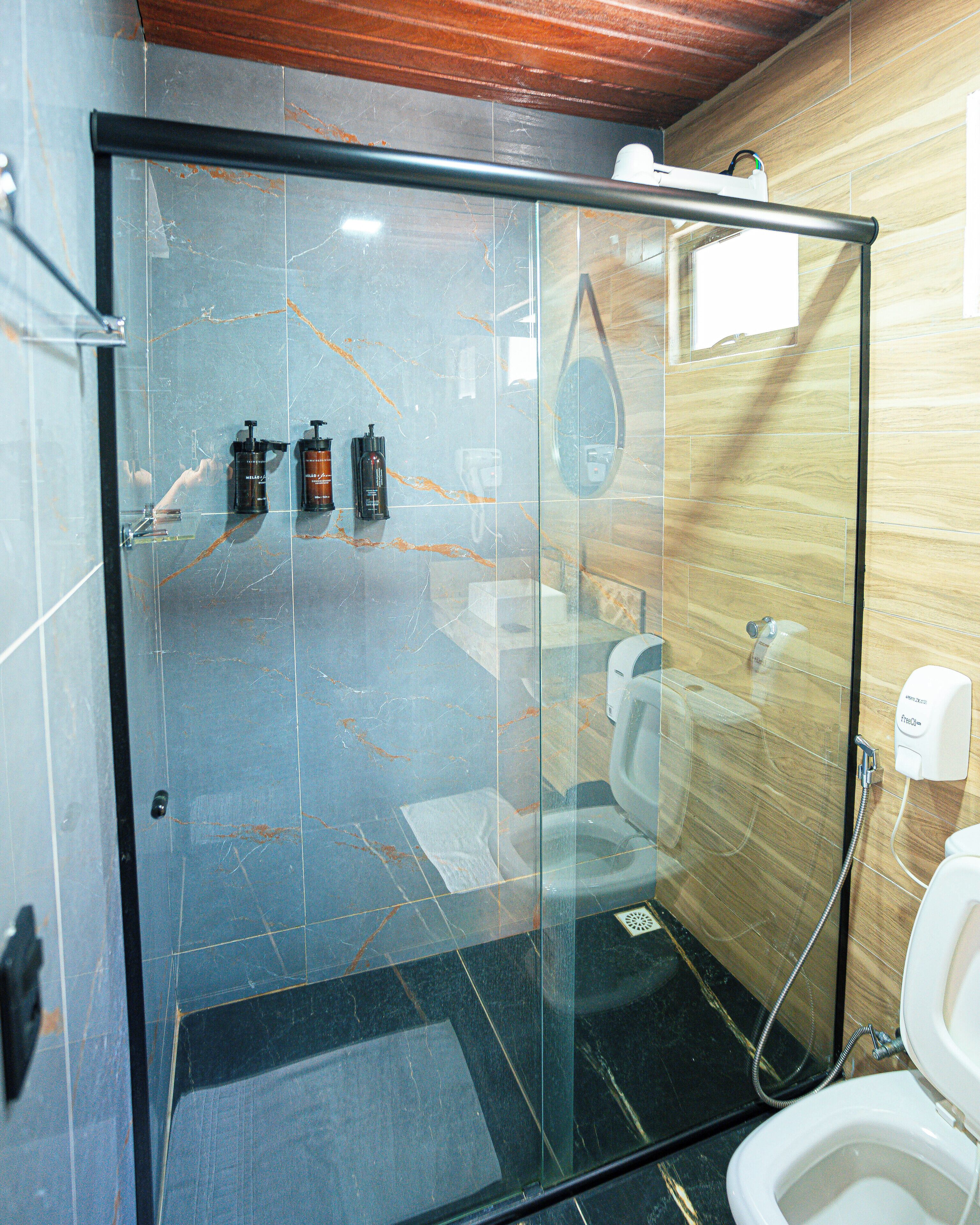 Cabina de ducha con paredes de vidrio, un inodoro y un secador de manos.
