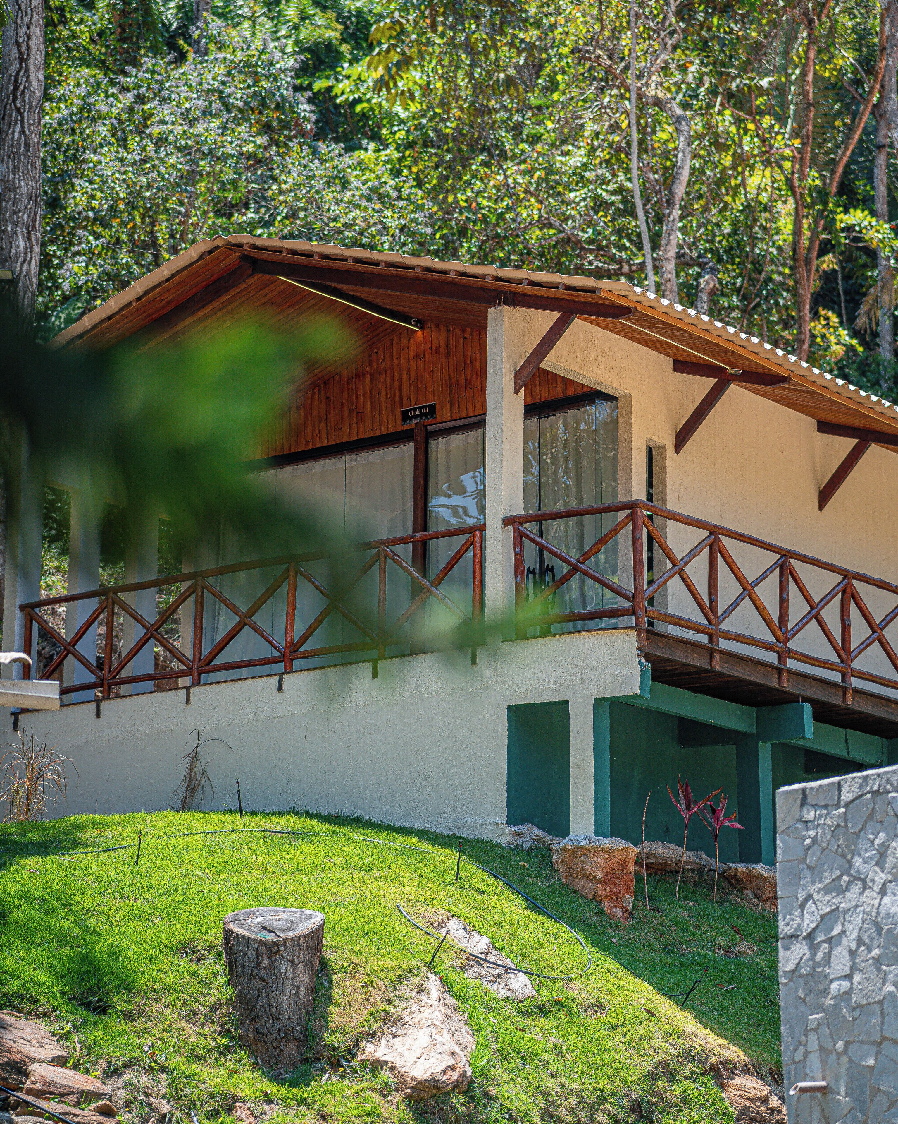A two-story building with a wooden balcony, a stone wall, and a grassy yard.