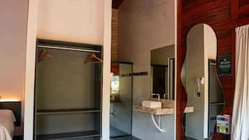 Un baño moderno con un espejo grande, una ducha y un lavabo. Hay un cubo con botellas en el suelo.