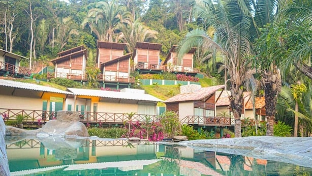 Ein Resort mit mehreren bungalowsartigen Unterkünften, einem zentral gelegenen Swimmingpool und üppiger tropischer Vegetation.