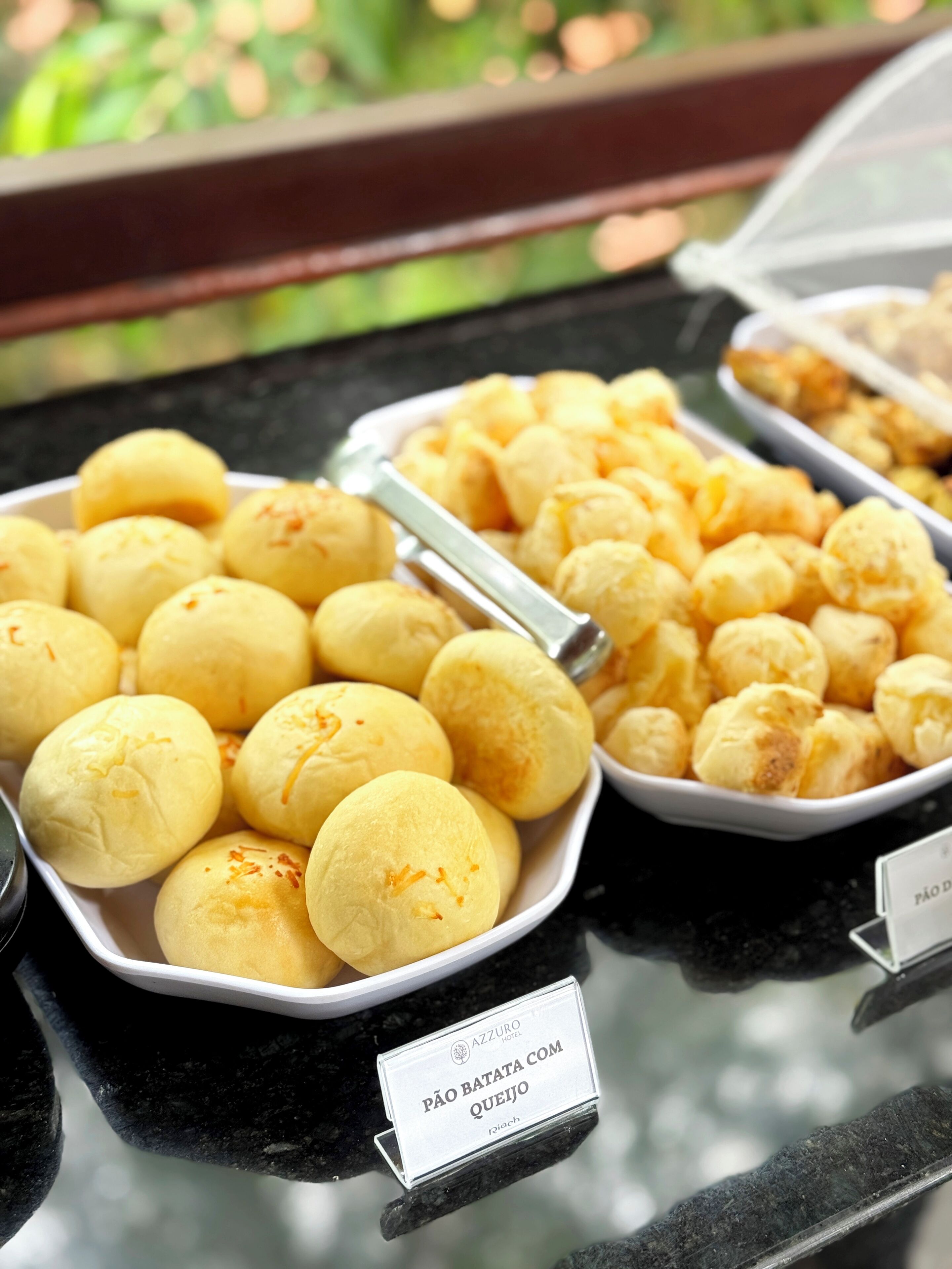 Buffet com diversos alimentos, incluindo uma placa que indica 'Pão Batata com Queijo'.