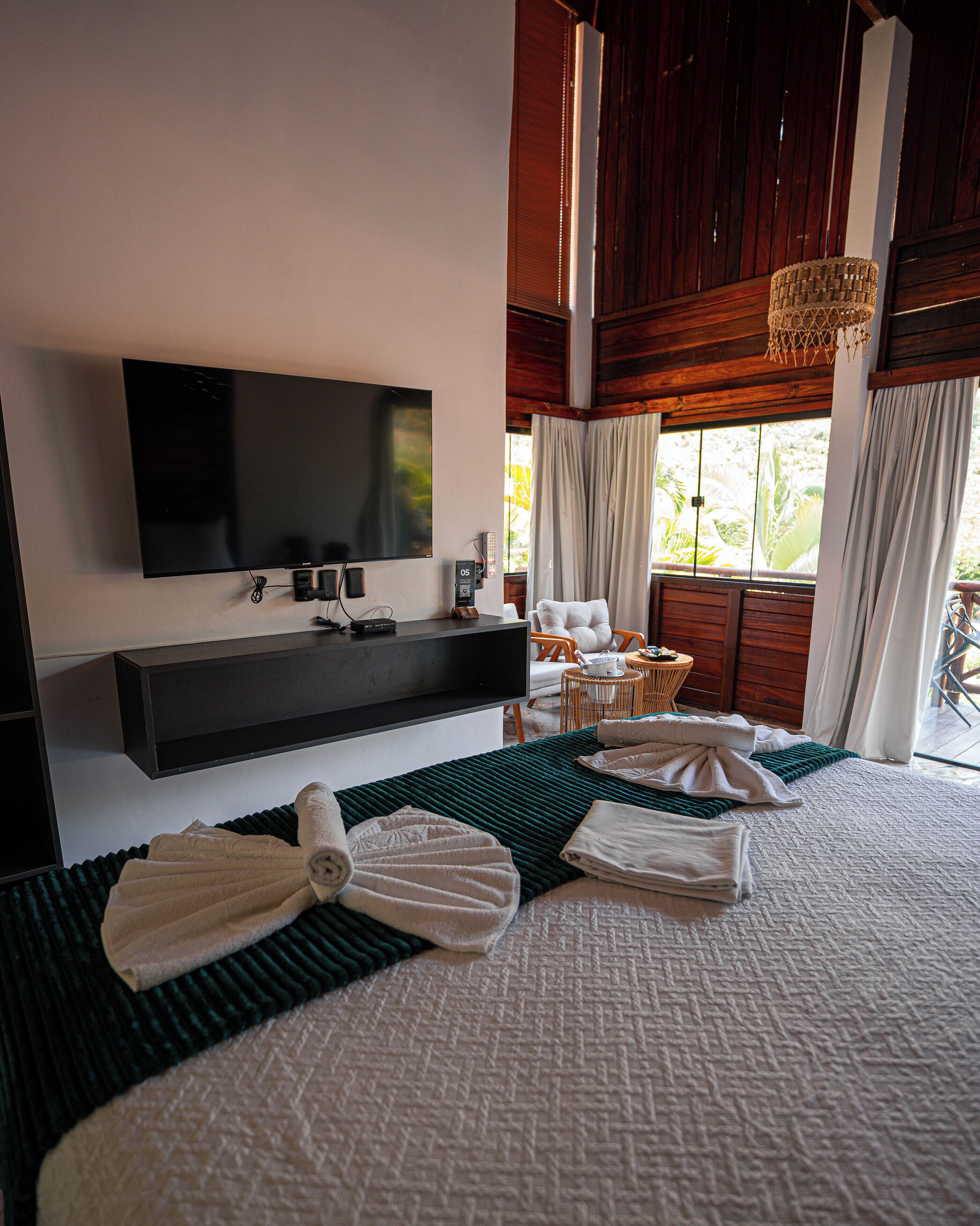 Habitación de hotel con una cama grande, un televisor de pantalla plana montado en la pared, techo de madera y vistas al exterior a través de la ventana.