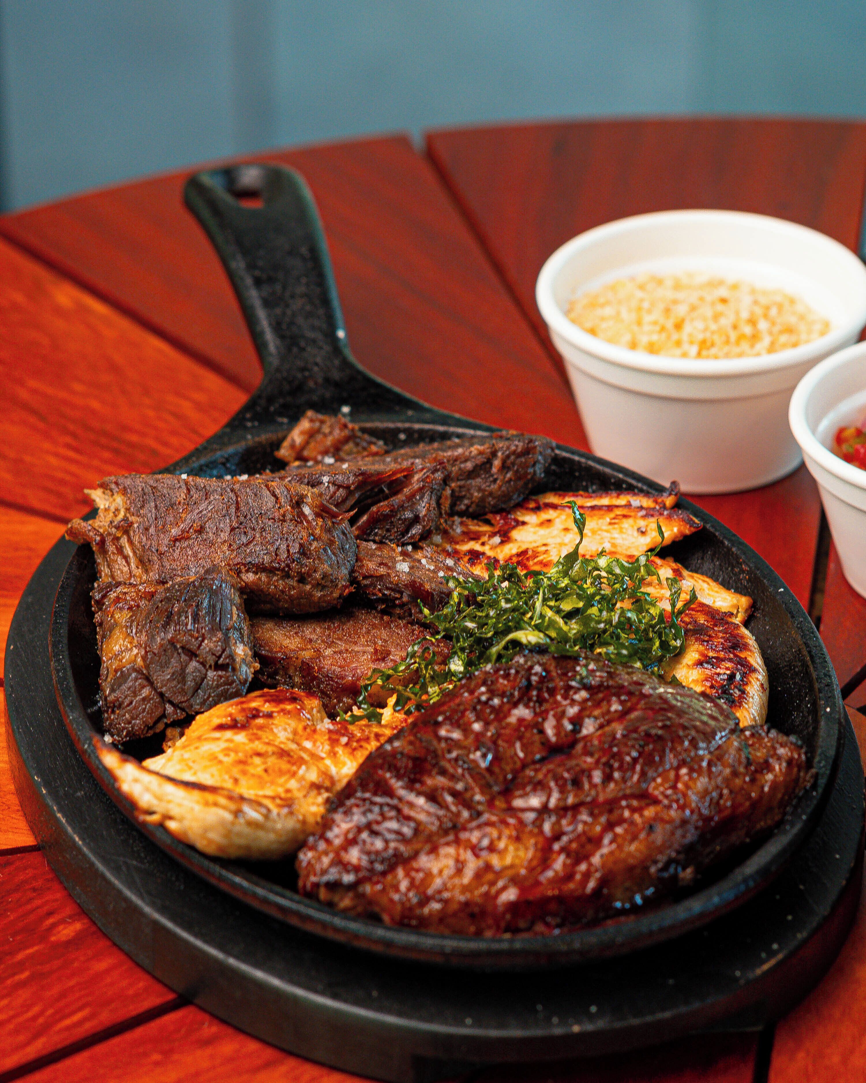 A cast iron skillet filled with various meats and vegetables on a wooden table.