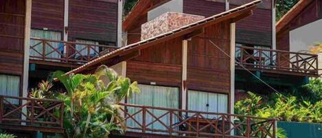 Un hotel de estilo cabaña con fachada de madera, varios balcones y exuberante vegetación tropical.