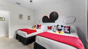 Une chambre avec deux lits, des murs en briques blanches et une décoration sur le thème de Mickey Mouse.