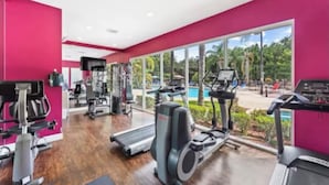 Une salle de sport équipée de machines de cardio, d’appareils de musculation et dotée d’une grande fenêtre donnant sur un espace piscine.