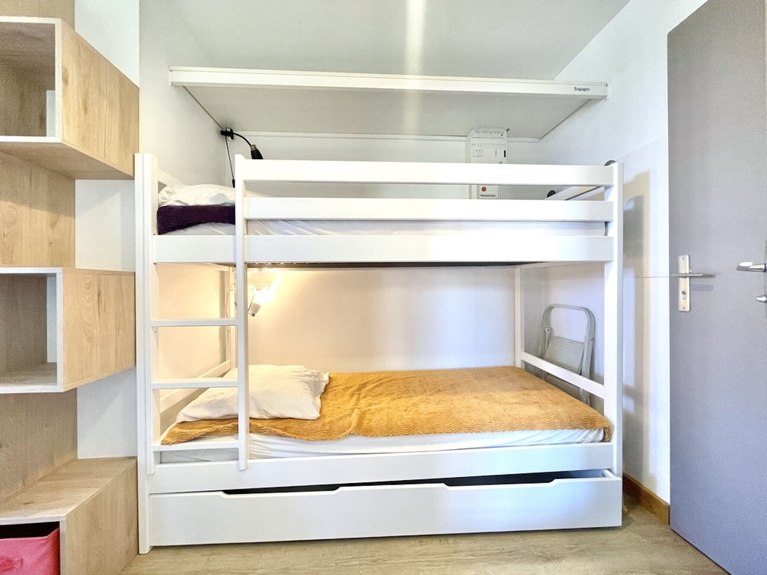 A bunk bed with a ladder, a shelf, and a door.