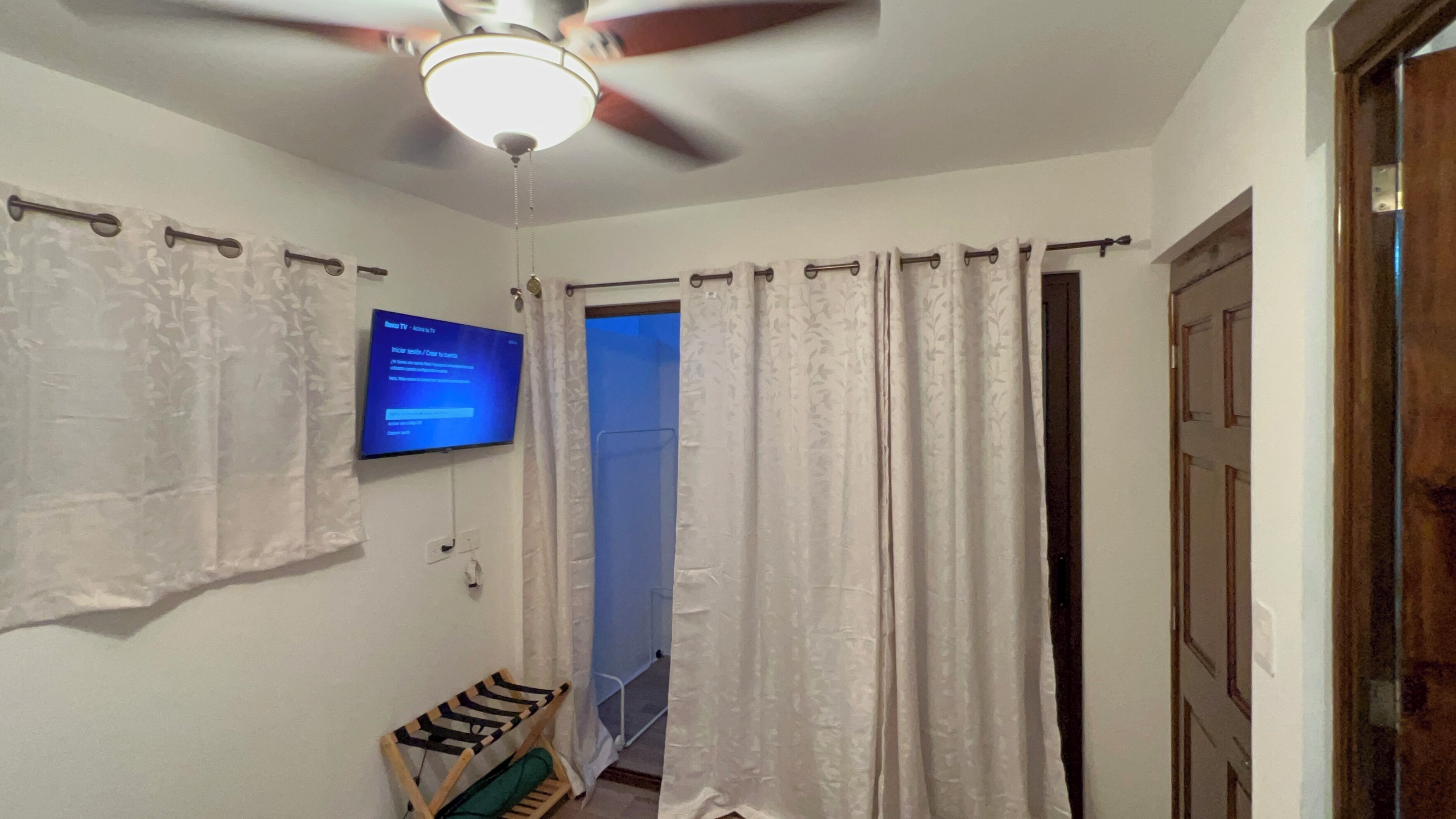 A room with a ceiling fan, a mounted TV displaying a login screen, and a door leading to another room.