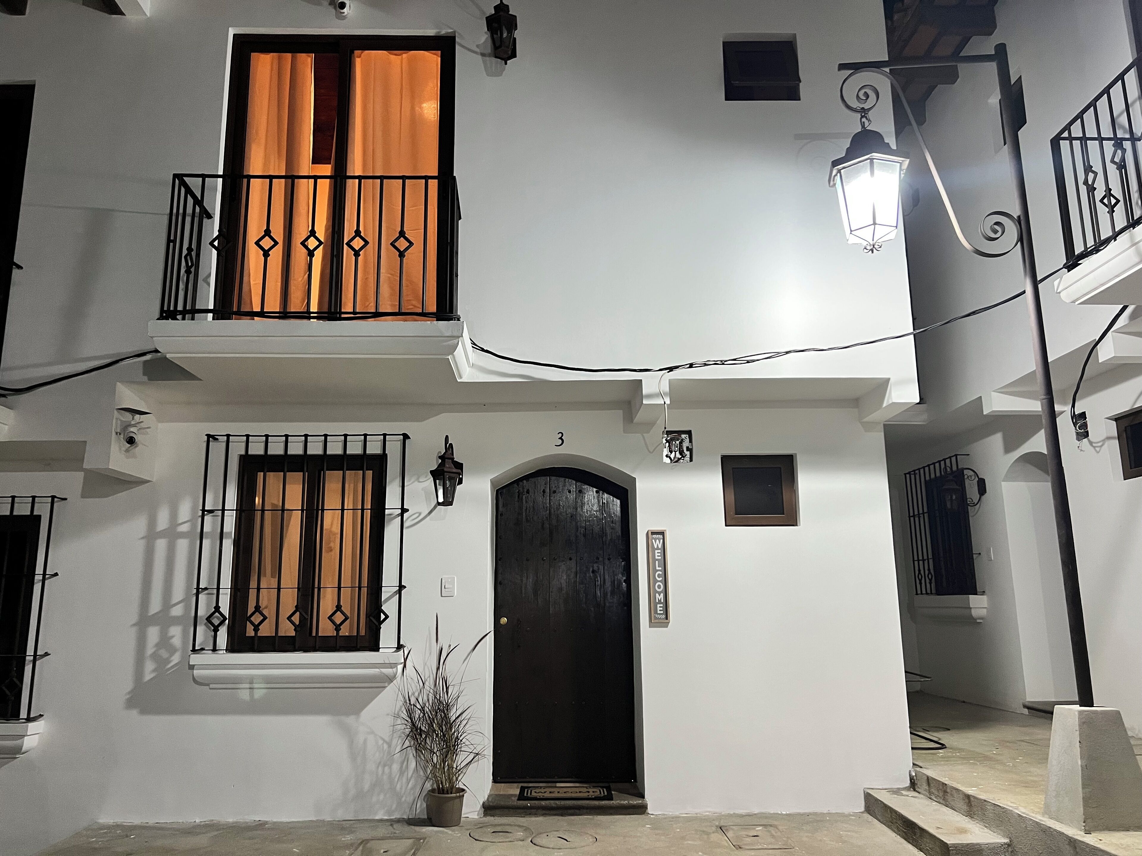 Un edificio con una puerta negra, un balcón con cortinas naranjas y un pequeño letrero que dice “BIENVENIDOS”.