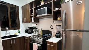 Moderni keittiö, jossa on puiset kaapit, ruostumattomasta teräksestä valmistettu jääkaappi, mikroaaltouuni ja liesi.