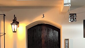 Tumma puuovi, jonka yläpuolella on numero 3, tervetulotoivotus, ruukussa oleva kasvi ja seinälle asennettu valaisin.