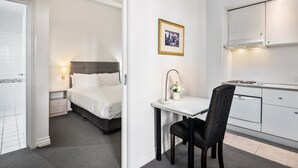 Ein kleines Hotelzimmer mit Bett, Nachttisch, Lampe und einem kleinen Schreibtisch mit Stuhl.