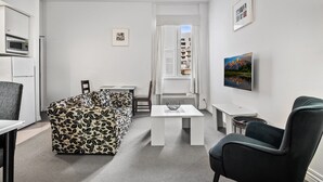 Ein gemütlicher Wohnraum mit einer Couch, einem Esstisch, einem Stuhl, einem kleinen Tisch mit einer Schüssel, einer Mikrowelle und einem an der Wand montierten Fernseher.