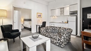 Ein modernes Hotelzimmer mit einer Couch, einem Esstisch, einer Küchenzeile inklusive Mikrowelle und einem Bett im angrenzenden Raum.