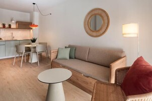 Una sala de estar moderna con un sofá, un espejo redondo, una mesa de comedor y una cocina al fondo.