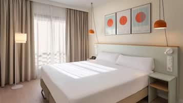 A hotel room with a large bed, a bedside table, a lamp, and a window with curtains.