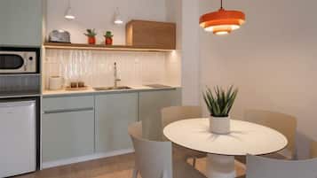 A modern kitchen with a built-in microwave, a sink, and a countertop with a toaster and potted plants. There is a round dining table with chairs and a hanging orange pendant light.