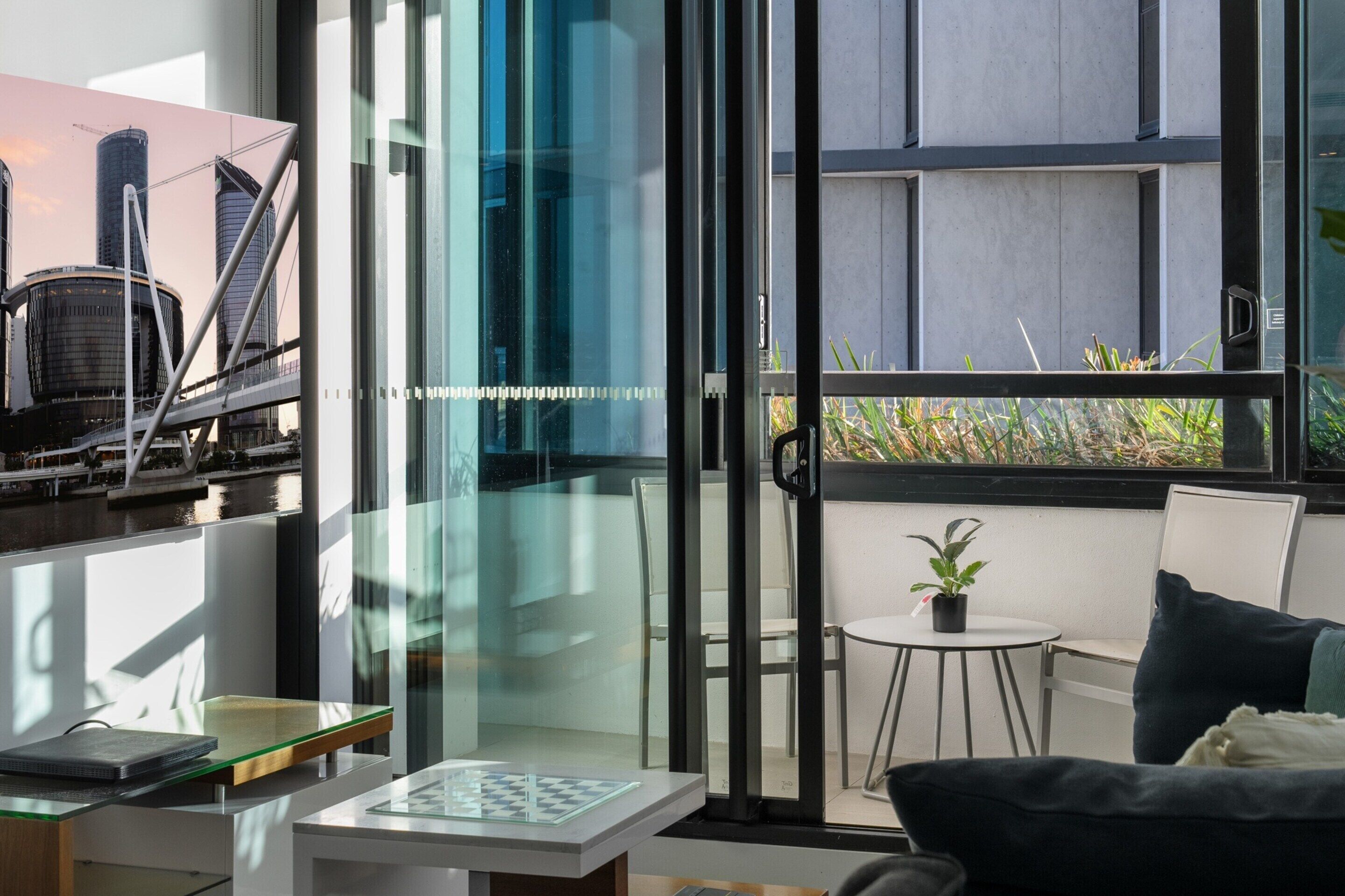 A modern room with a glass door leading to a balcony, a small table with a plant, and a sofa.