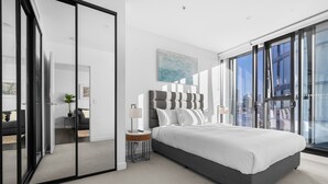 A modern bedroom with a large bed, a bedside table, a lamp, and a view through floor-to-ceiling windows. - City Escape With Balcony & Resort-style Amenities (Brisbane)