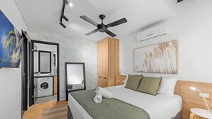 Quarto de hotel moderno com uma cama grande, um ventilador de teto, um aparelho de ar condicionado, uma máquina de lavar e um espelho.