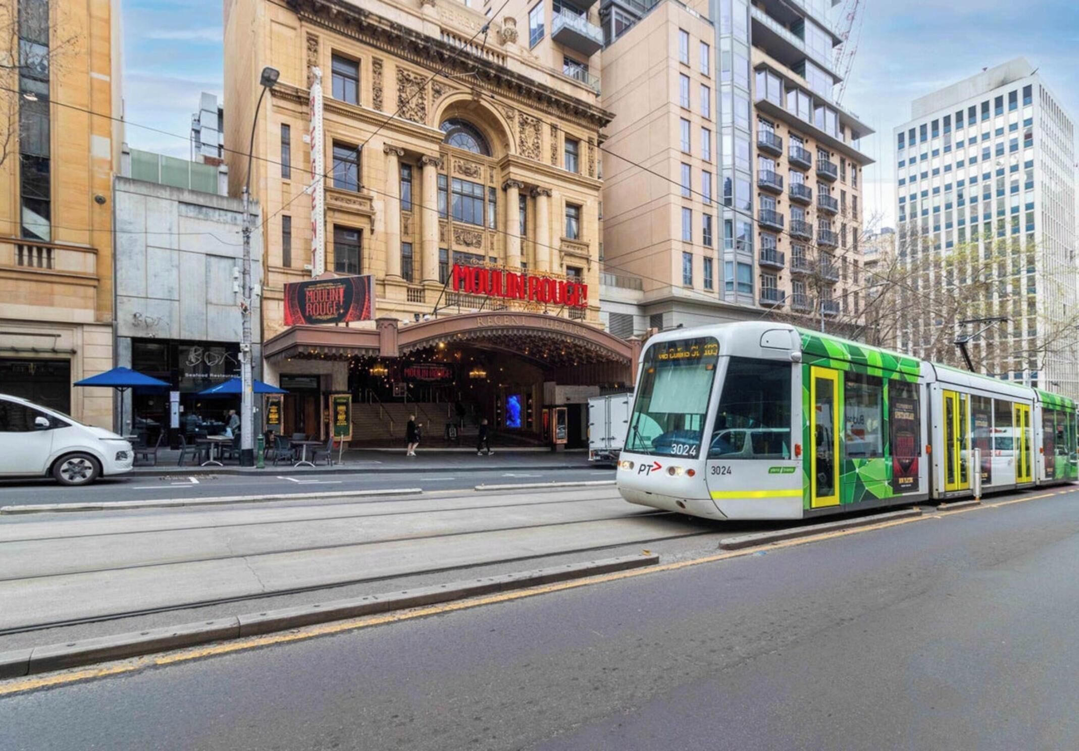 A tram on a city street with a building featuring a marquee sign reading "MAIN ROYAL" and a restaurant named "BORDEN ROOF" in front.